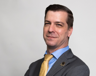 Portrait of a smiling Chase Oliver wearing a grey suite, a light blue shirt, and a yellow tie.